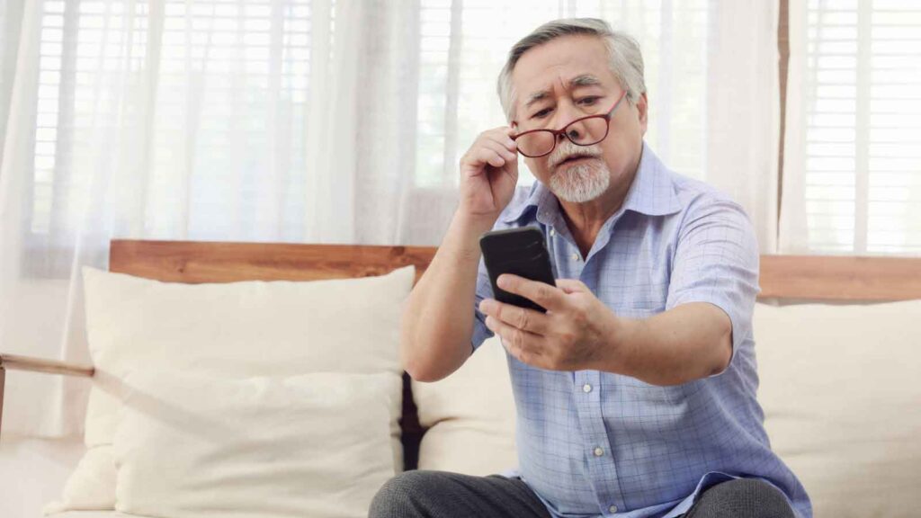 Older man struggles to read phone screen while adjusting glasses