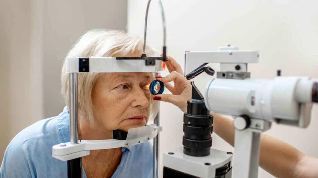  Older woman receives an eye exam using a slit lamp device.